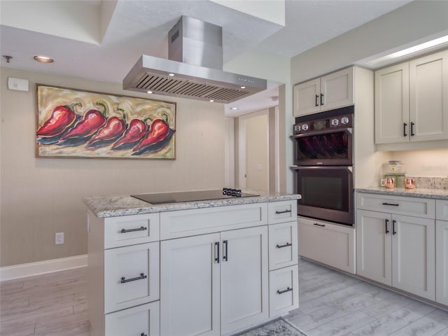 123 Tidy Island Blvd, Bradenton, FL 34210 - kitchen with wall chimney range hood, double oven, light wood-type flooring, black electric cooktop, and light stone countertops