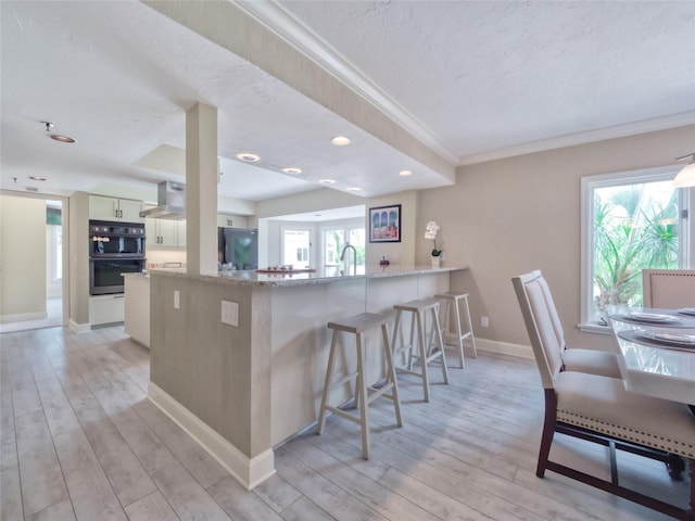 123 Tidy Island Blvd, Bradenton, FL 34210 - kitchen featuring crown molding, light wood-style floors, wall chimney exhaust hood, a breakfast bar area, and fridge