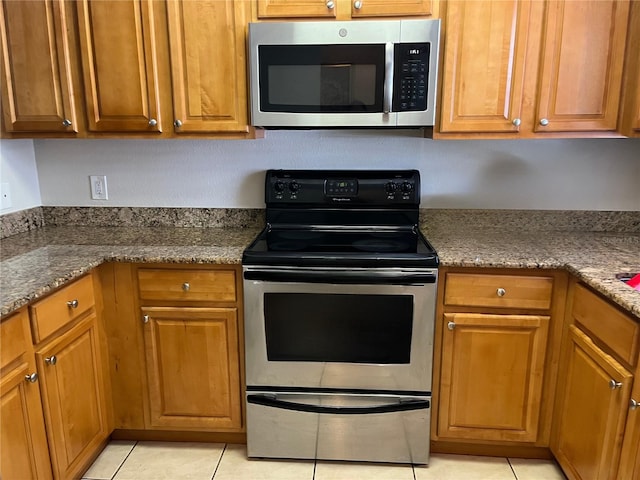 900 La Costa Cir Unit 4, Sarasota, FL 34237 - kitchen with appliances with stainless steel finishes, light tile patterned floors, brown cabinetry, and stone countertops