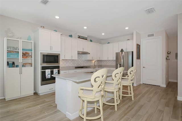 16231 Tradewind Ter, Bradenton, FL 34211 - kitchen with stainless steel appliances, under cabinet range hood, light wood-style floors, light countertops, and decorative backsplash