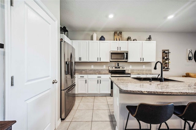 8979 Milestone Dr, Sarasota, FL 34238 - kitchen with stainless steel appliances, a kitchen bar, white cabinetry, light tile patterned flooring, and light stone counters