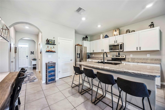 8979 Milestone Dr, Sarasota, FL 34238 - kitchen with stainless steel appliances, arched walkways, a kitchen bar, white cabinets, and light tile patterned floors