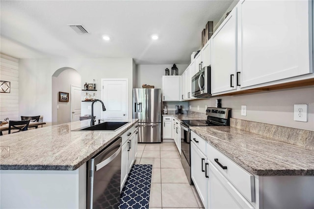 8979 Milestone Dr, Sarasota, FL 34238 - kitchen with stainless steel appliances, arched walkways, a center island with sink, white cabinetry, and light tile patterned floors