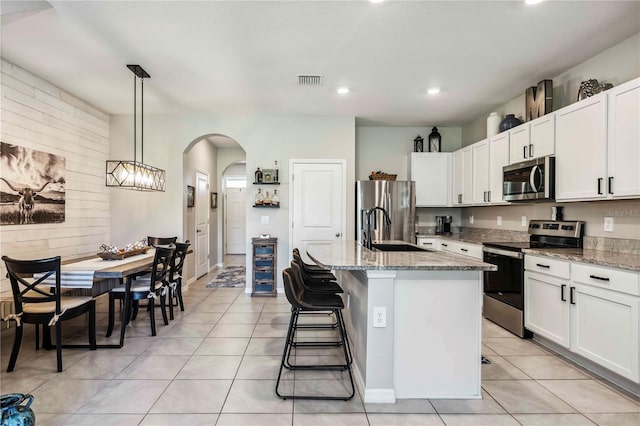 8979 Milestone Dr, Sarasota, FL 34238 - kitchen with stainless steel appliances, arched walkways, light stone counters, a center island with sink, and white cabinetry