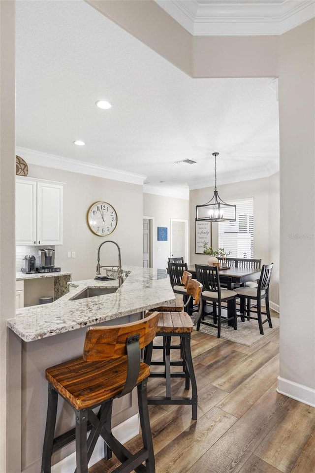 8840 Brookfield Ter, Bradenton, FL 34212 - kitchen with a kitchen bar, crown molding, light wood-type flooring, light stone countertops, and white cabinets