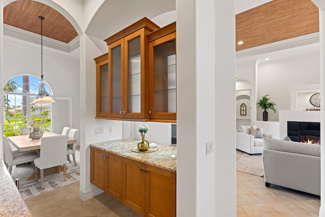 7144 Ashland Gln, Lakewood Ranch, FL 34202 - bar area featuring light tile patterned floors, ornamental molding, a raised ceiling, hanging light fixtures, and a lit fireplace