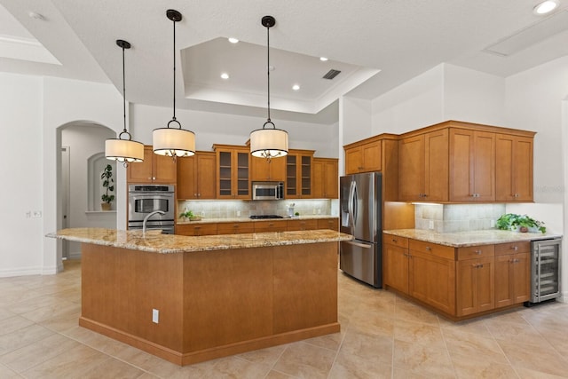 7144 Ashland Gln, Lakewood Ranch, FL 34202 - kitchen featuring appliances with stainless steel finishes, wine cooler, brown cabinetry, arched walkways, and recessed lighting