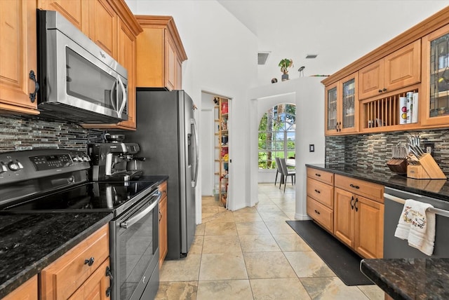 6805 225th St E, Bradenton, FL 34211 - kitchen with appliances with stainless steel finishes, backsplash, glass insert cabinets, dark stone countertops, and brown cabinets