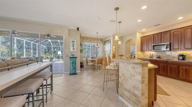 7915 Kavanagh Ct, Sarasota, FL 34240 - kitchen with stainless steel microwave, a kitchen breakfast bar, a sunroom, light tile patterned flooring, and crown molding