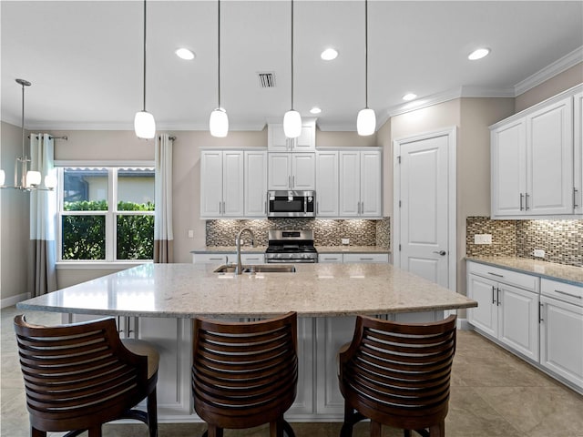 5364 Salcano St, Sarasota, FL 34238 - kitchen with stainless steel appliances, crown molding, a center island with sink, white cabinets, and decorative backsplash