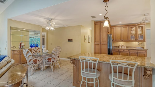 7426 Weeping Willow Blvd, Sarasota, FL 34241 - kitchen featuring a ceiling fan, a kitchen bar, freestanding refrigerator, light tile patterned floors, and brown cabinetry