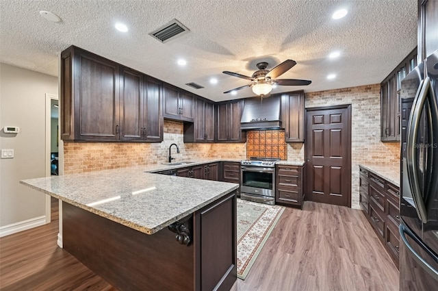 1509 Shadow Ridge Cir, Sarasota, FL 34240 - kitchen featuring appliances with stainless steel finishes, wall chimney exhaust hood, a peninsula, dark brown cabinetry, and light wood-style floors