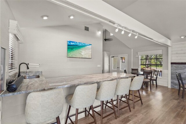 4333 Trails Dr Unit 10-1, Sarasota, FL 34232 - kitchen featuring lofted ceiling, rail lighting, wood finished floors, light stone countertops, and a breakfast bar area