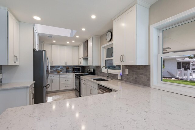 3715 101st St W, Bradenton, FL 34210 - kitchen featuring stainless steel appliances, a skylight, tasteful backsplash, light stone counters, and white cabinetry