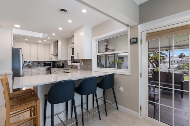 3715 101st St W, Bradenton, FL 34210 - kitchen with stainless steel appliances, decorative backsplash, white cabinets, a skylight, and a peninsula