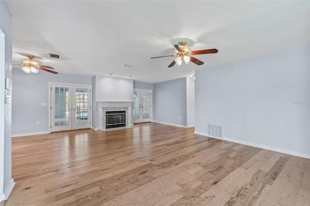 6103 6th Ave NW, Bradenton, FL 34209 - unfurnished living room featuring ceiling fan, light wood-type flooring, a textured ceiling, a fireplace, and french doors
