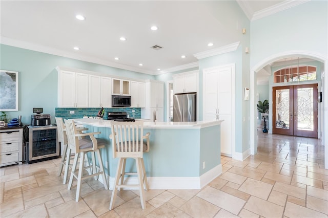 7521 Aralia Way, Seminole, FL 33777 - kitchen featuring beverage cooler, appliances with stainless steel finishes, backsplash, a kitchen island with sink, and french doors