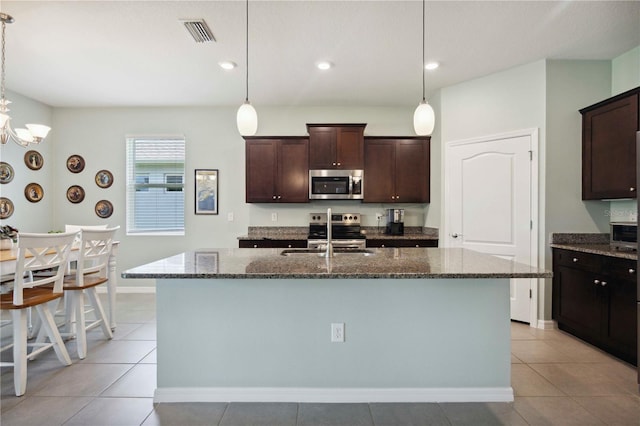 13804 Woodbridge Ter, Lakewood Ranch, FL 34211 - kitchen featuring stainless steel appliances, dark stone counters, dark brown cabinetry, a kitchen island with sink, and recessed lighting