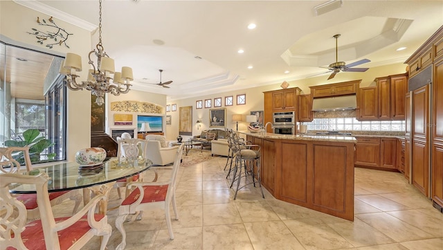 8832 Enclave Ct, Sarasota, FL 34238 - kitchen featuring ceiling fan, a raised ceiling, ornamental molding, under cabinet range hood, and brown cabinets