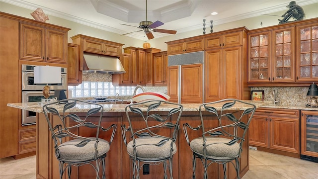 8832 Enclave Ct, Sarasota, FL 34238 - kitchen with stainless steel appliances, brown cabinets, under cabinet range hood, light stone counters, and a ceiling fan