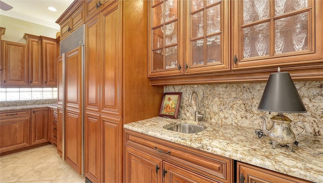 8832 Enclave Ct, Sarasota, FL 34238 - kitchen with brown cabinetry, light stone counters, tasteful backsplash, glass insert cabinets, and crown molding