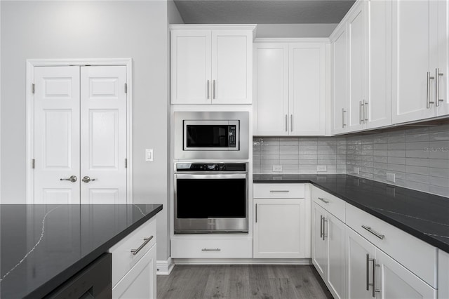 8706 Arrow Creek Dr, Parrish, FL 34219 - kitchen featuring stainless steel appliances, light wood-type flooring, white cabinets, tasteful backsplash, and dark stone countertops
