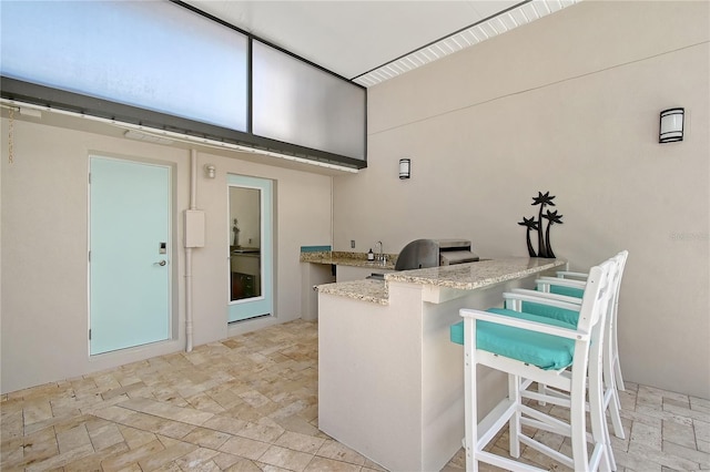 444 S Polk Dr, Sarasota, FL 34236 - kitchen featuring a breakfast bar, light stone finish floors, a peninsula, and light stone countertops