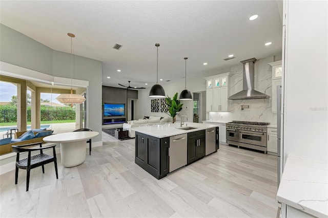 12814 Daisy Pl, Bradenton, FL 34212 - kitchen featuring stainless steel appliances, wall chimney range hood, tasteful backsplash, open floor plan, and a kitchen island with sink