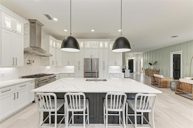 12814 Daisy Pl, Bradenton, FL 34212 - kitchen with wall chimney exhaust hood, appliances with stainless steel finishes, tasteful backsplash, light wood finished floors, and a center island with sink