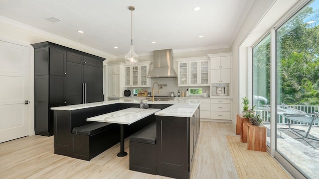 1076 Toc0Baga, Sarasota, FL 34234 - kitchen with wall chimney range hood, a large island with sink, white cabinets, light wood-type flooring, and glass insert cabinets