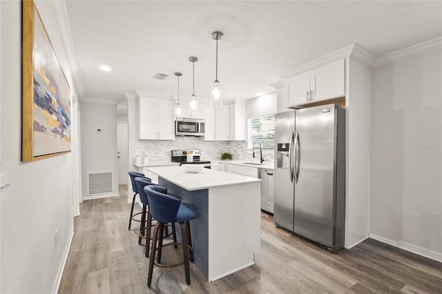 1008 37th St W, Bradenton, FL 34205 - kitchen featuring stainless steel appliances, white cabinets, ornamental molding, decorative backsplash, and a kitchen island