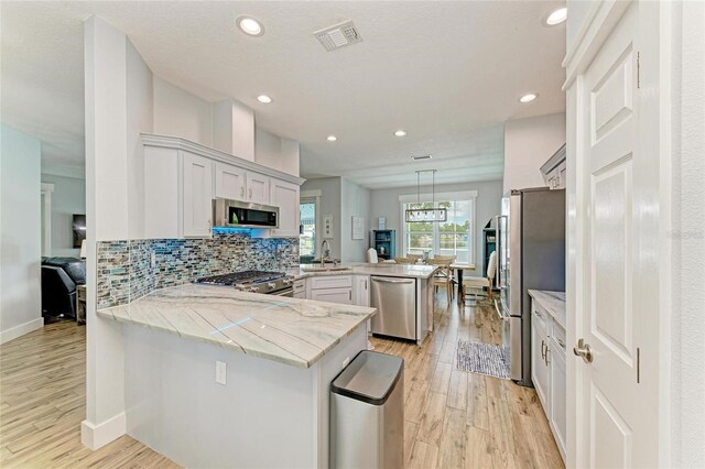 220 39th St NE, Bradenton, FL 34208 - kitchen featuring stainless steel appliances, a peninsula, light stone countertops, light wood-style floors, and tasteful backsplash