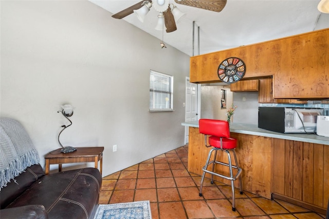 15780 Wilson Rd, Sarasota, FL 34240 - kitchen with brown cabinetry, ceiling fan, a peninsula, light countertops, and a kitchen breakfast bar