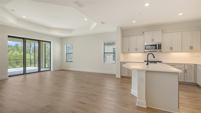 248 Altamura Cir, Nokomis, FL 34275 - kitchen featuring stainless steel microwave, a raised ceiling, light countertops, tasteful backsplash, and light wood finished floors