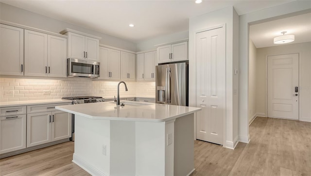 248 Altamura Cir, Nokomis, FL 34275 - kitchen featuring appliances with stainless steel finishes, light wood-style floors, light countertops, backsplash, and a center island with sink
