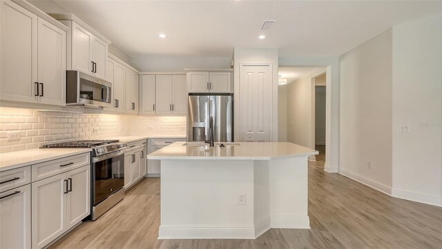 248 Altamura Cir, Nokomis, FL 34275 - kitchen with stainless steel appliances, light wood-style flooring, decorative backsplash, a center island with sink, and recessed lighting
