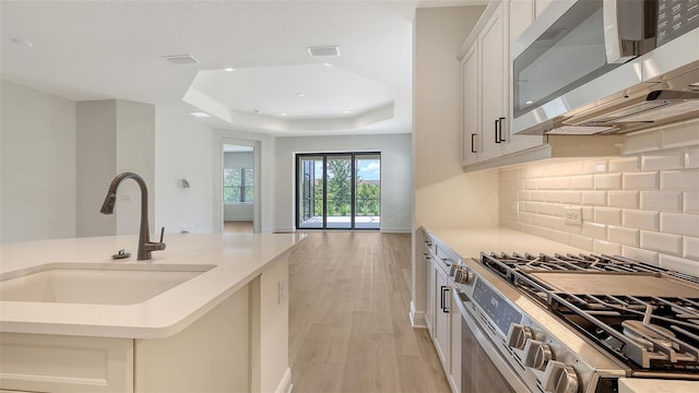 248 Altamura Cir, Nokomis, FL 34275 - kitchen with stainless steel appliances, a raised ceiling, light wood-style floors, backsplash, and light countertops