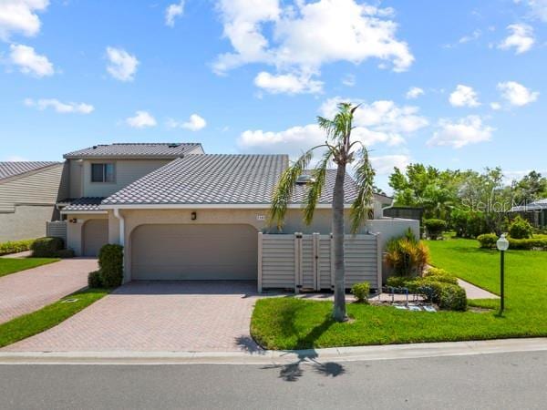 2181 Harbourside Dr Unit 1403, Longboat Key, FL 34228 - view of front of house featuring decorative driveway, an attached garage, a tile roof, a front yard, and stucco siding