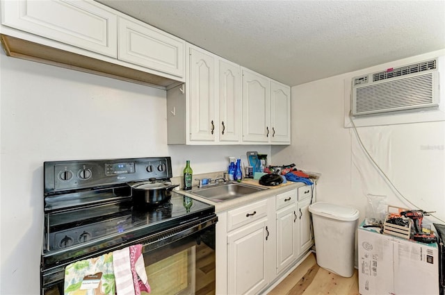1701 13th St W, Bradenton, FL 34205 - kitchen featuring black electric range oven, a wall mounted AC, white cabinetry, light wood finished floors, and a textured ceiling