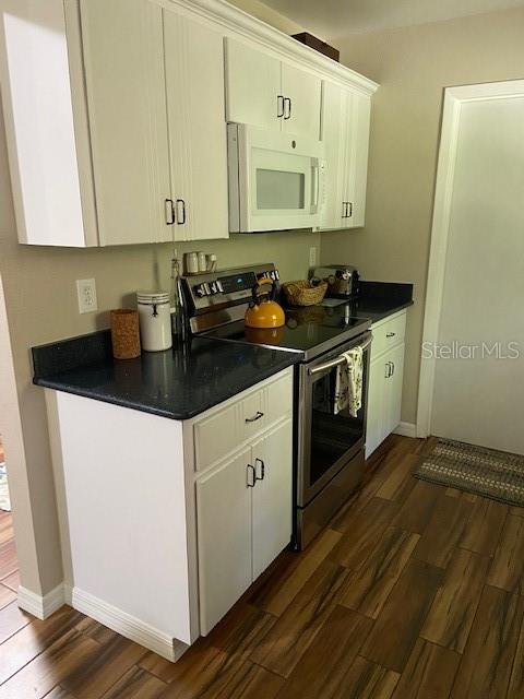 3683 Brown, Arcadia, FL 34266 - kitchen with white microwave, stainless steel electric range, dark wood-style flooring, dark countertops, and white cabinets