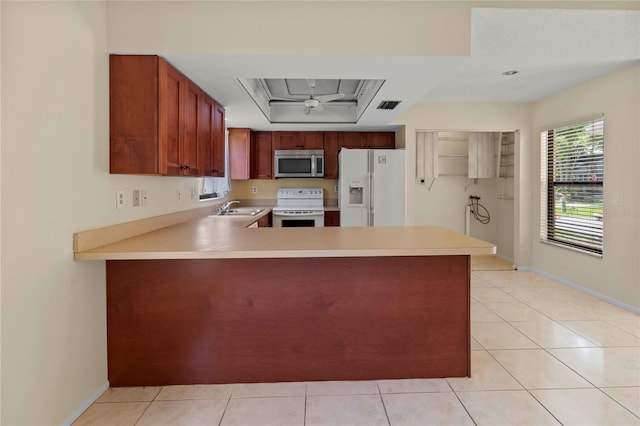 4805 Cypress Lake Ct, Sarasota, FL 34243 - kitchen with white appliances, a tray ceiling, a peninsula, light countertops, and light tile patterned floors