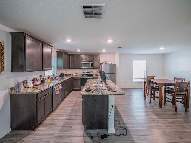 938 Mansfield Rd, Tavares, FL 32778 - kitchen featuring appliances with stainless steel finishes, dark brown cabinets, a kitchen island, light stone counters, and recessed lighting
