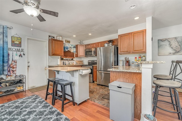 4481 Lagg Ave, Fort Myers, FL 33901 - kitchen featuring appliances with stainless steel finishes, a kitchen breakfast bar, light wood finished floors, a ceiling fan, and brown cabinets
