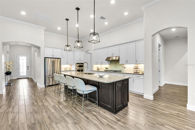 3379 Chestertown Loop, Bradenton, FL 34211 - kitchen with stainless steel appliances, arched walkways, white cabinets, a large island with sink, and ornamental molding