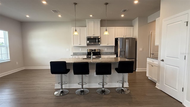 14312 Crimson Ave, Bradenton, FL 34211 - kitchen featuring appliances with stainless steel finishes, dark wood-style flooring, an island with sink, white cabinets, and a kitchen breakfast bar