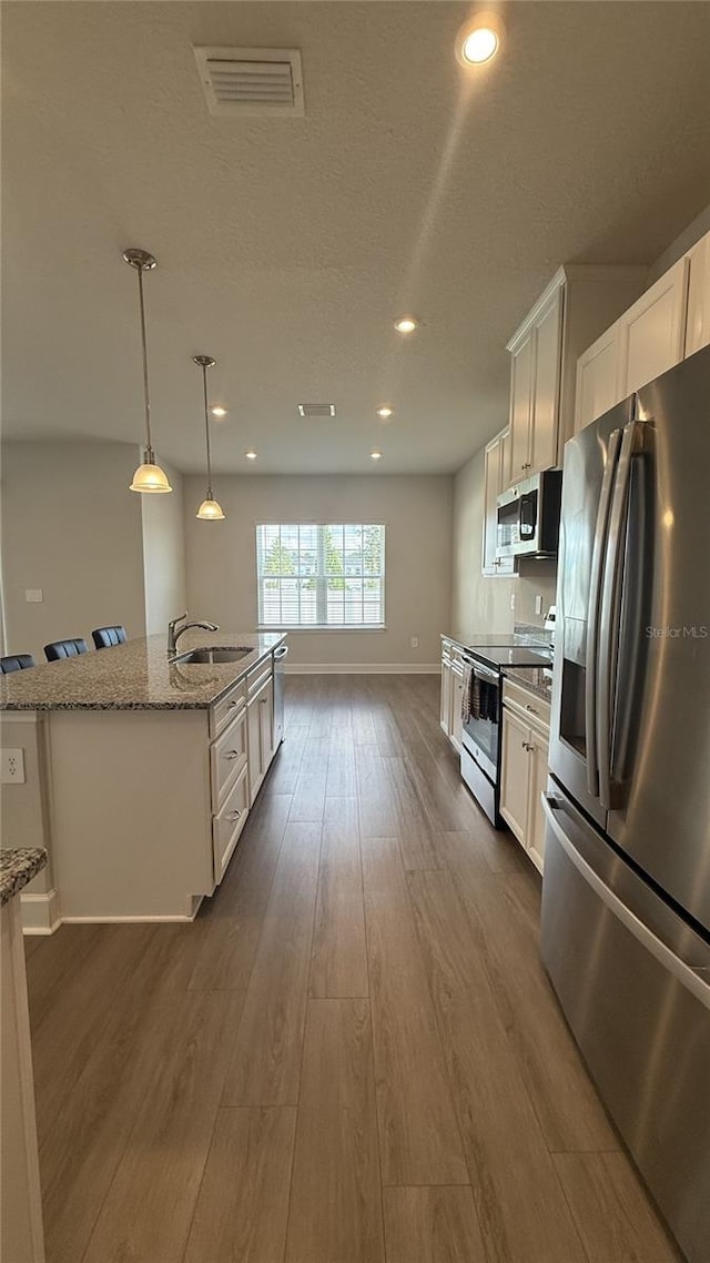 14312 Crimson Ave, Bradenton, FL 34211 - kitchen featuring appliances with stainless steel finishes, dark wood finished floors, white cabinetry, an island with sink, and light stone counters