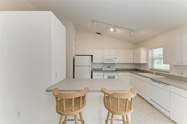 7824 48th Pl E, Bradenton, FL 34203 - kitchen featuring white appliances, track lighting, a kitchen breakfast bar, vaulted ceiling, and a peninsula