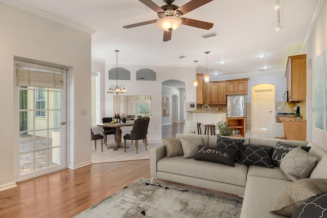 12113 Whistling Way, Lakewood Ranch, FL 34202 - living room featuring arched walkways, crown molding, a ceiling fan, light wood finished floors, and a chandelier
