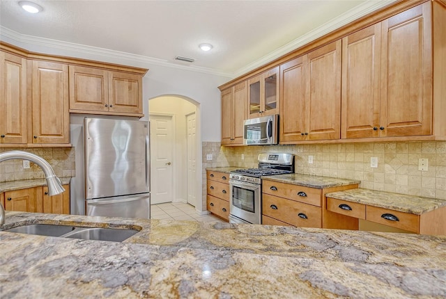 12113 Whistling Way, Lakewood Ranch, FL 34202 - kitchen with stainless steel appliances, light stone countertops, arched walkways, ornamental molding, and glass insert cabinets