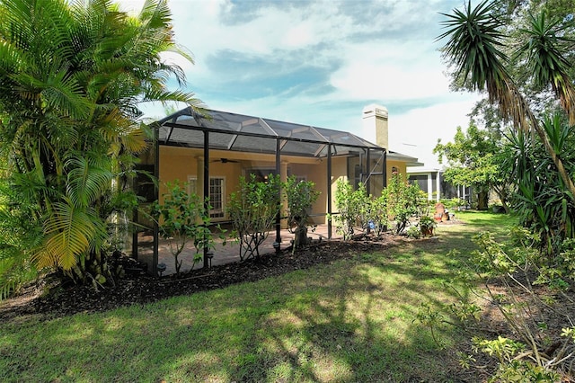 12113 Whistling Way, Lakewood Ranch, FL 34202 - back of house featuring a ceiling fan, a lawn, a patio area, stucco siding, and glass enclosure